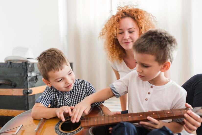 Activités de Noël : femme regardant ses enfants jouant de la guitare.